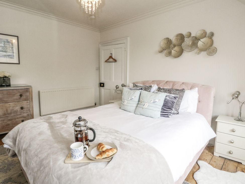 A bedroom with a bed, bedside table, dresser and a tray with a mug and croissants at Rowan Tree House in Brechin