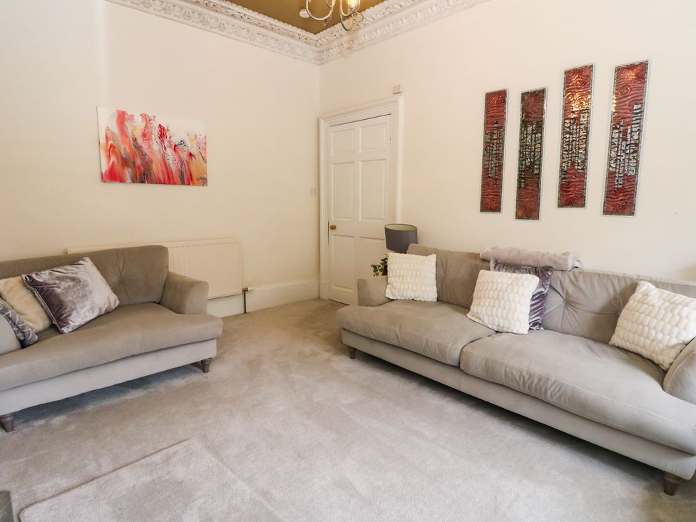 A living room with two sofas, a painting, and a door at Rowan Tree House in Brechin