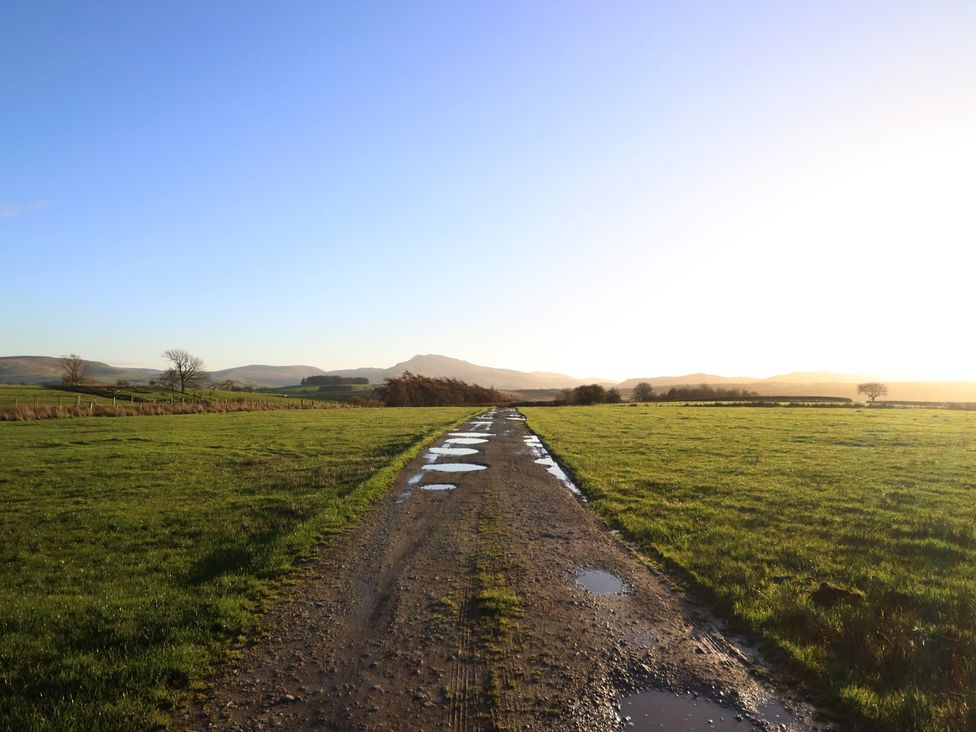 A dirt road with puddles leading through grass fields at 1 Fron Uchaf, Parc near Bala