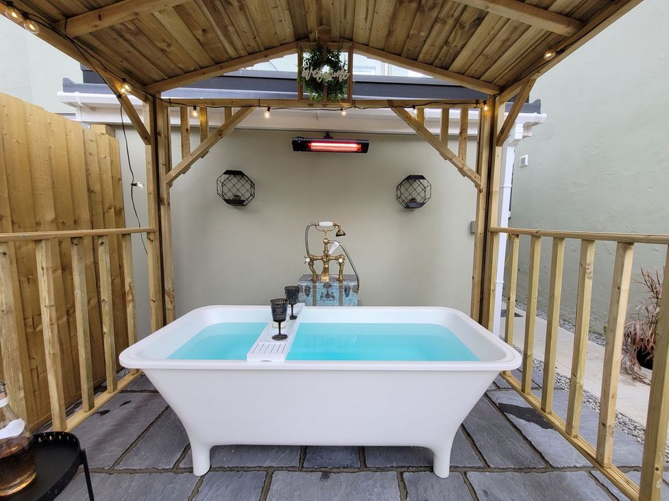 An outdoor bath area with a bathtub under a wooden structure at Klysa in Camborne