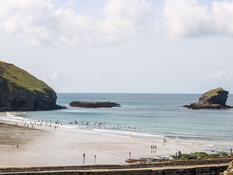 A beach with people wading in the water and hills in the background at Teylu in Camborne