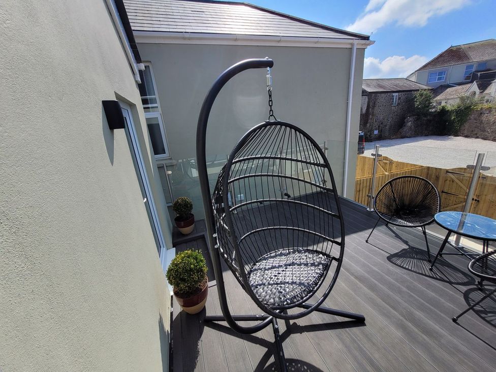An outdoor deck with a hanging chair and table at Daniel Chambers in Camborne