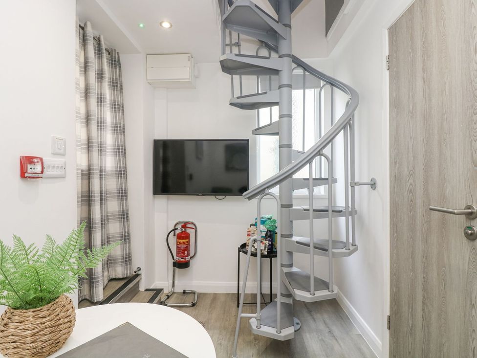 A snug with a spiral staircase and a television at The Snug in Camborne