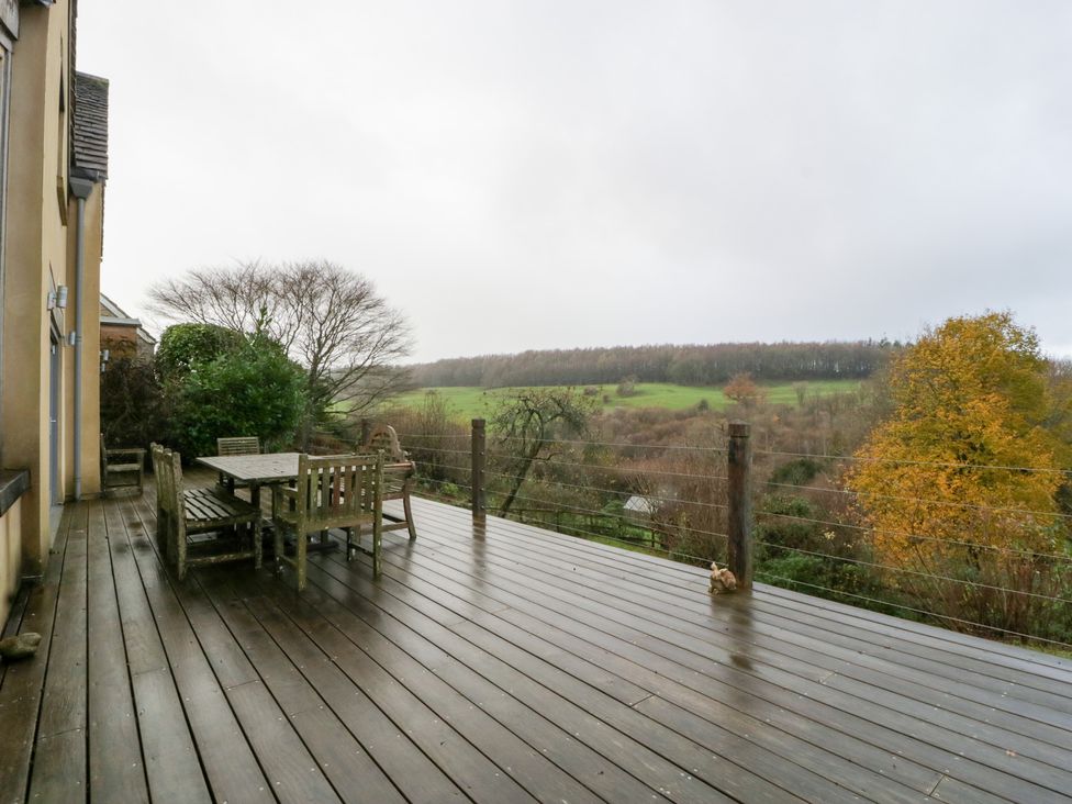 An outdoor deck with a table and chairs overlooking hills at Spring View in Tetbury