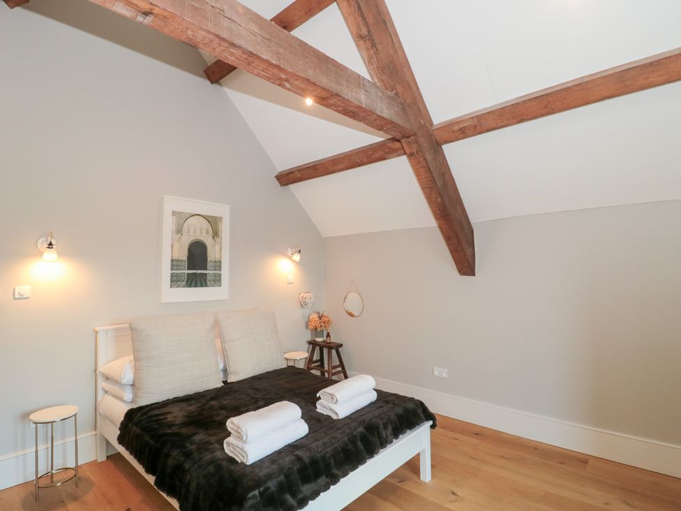 A bedroom with a bed, table, and wooden beams at Spring View in Kingscote, Gloucestershire