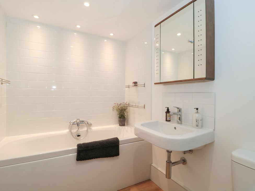 A bathroom with a bathtub, sink, and mirror at Spring View in Kingscote, Gloucestershire