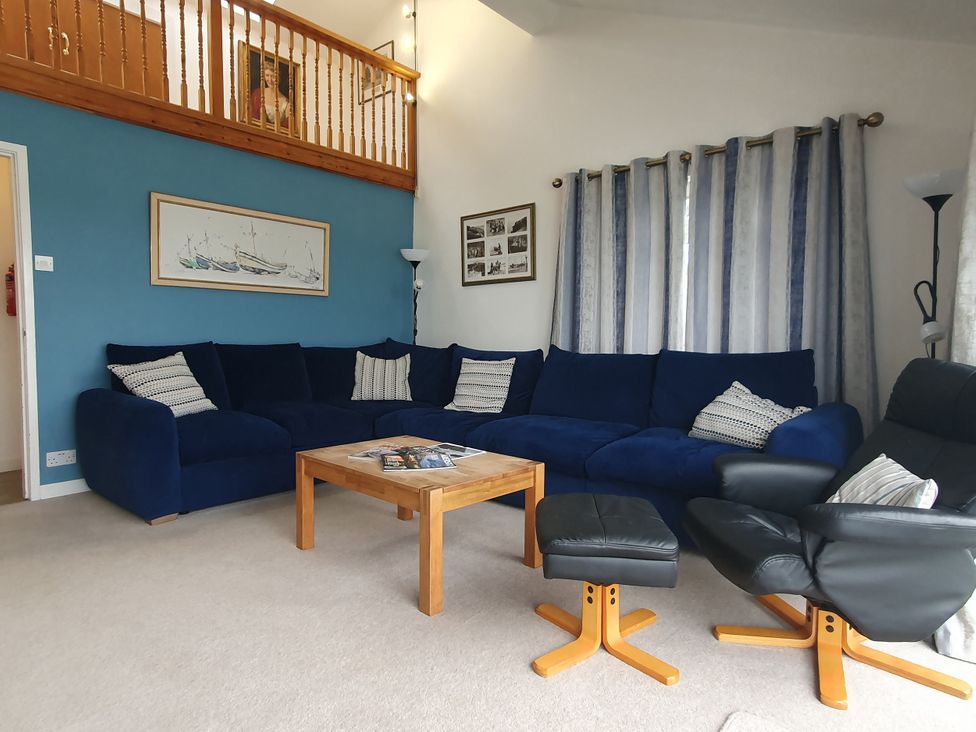 A living room with a blue sofa and wooden coffee table at Gilfach Goed in Pwllheli