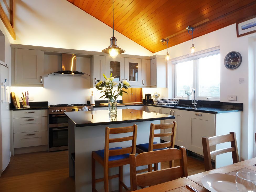 A kitchen with an island and stools at Gilfach Goed in Pwllheli
