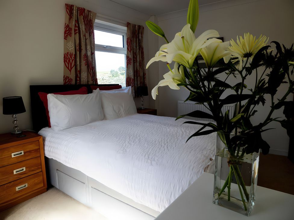 A bedroom with a bed and flowers on a table at Gilfach Goed Pwllheli