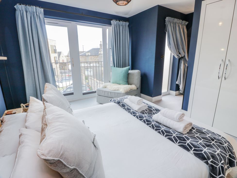 A bedroom with a bed, towels, and an armchair at 14 Old Market Place Bonnyrigg