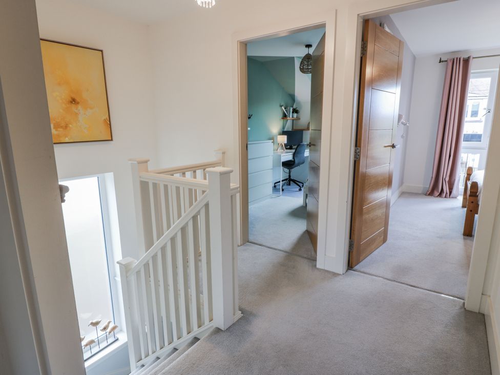A hallway with a staircase, artwork, and doors leading to rooms at 14 Old Market Place in Bonnyrigg