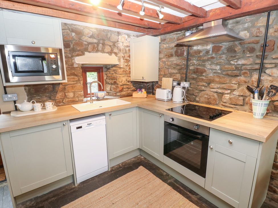 A kitchen with stone walls and modern appliances at Melyn Aberdare
