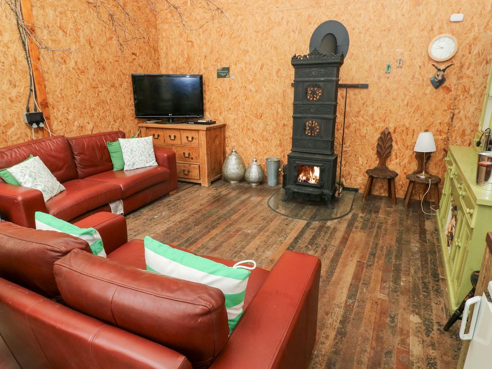 A living room with a sofa, television, wooden chest, and stove at Melyn in Aberdare