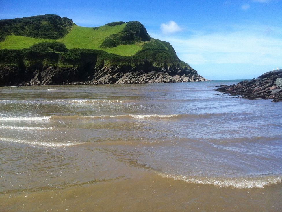 A coastal scene with waves and a grassy hill at Round Barn in Ilfracombe