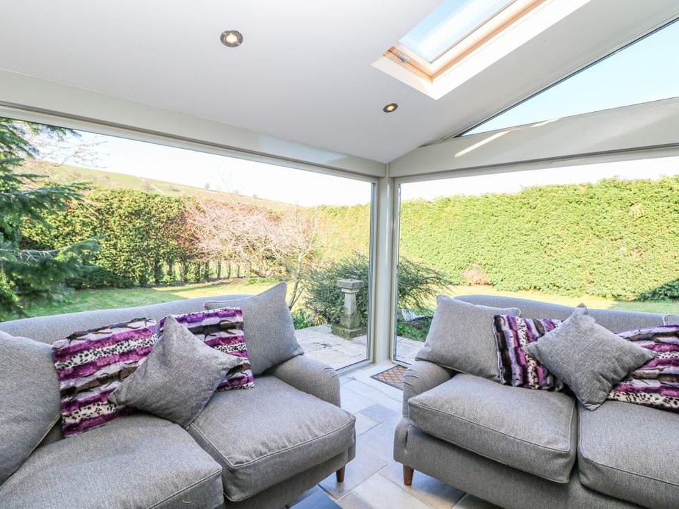 A conservatory with sofas overlooking a garden at Peters Lea in Bakewell