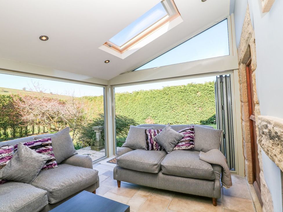 A conservatory with a sofa and cushions at Peters Lea, Bakewell