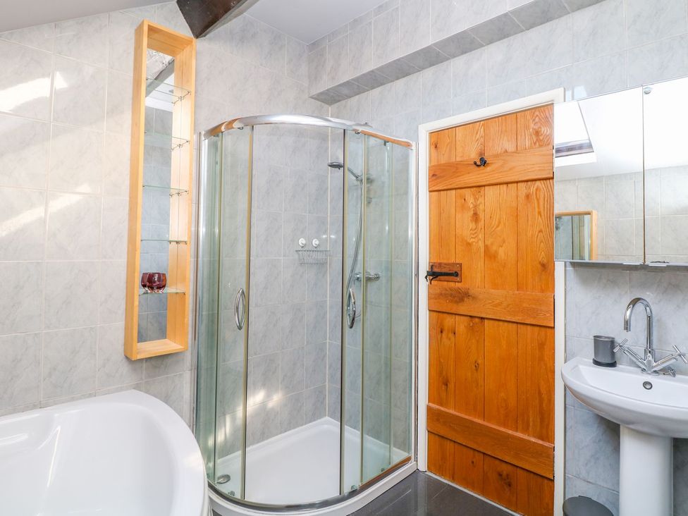 A bathroom with a shower, bathtub, sink, and wooden door at Peters Lea in Bakewell