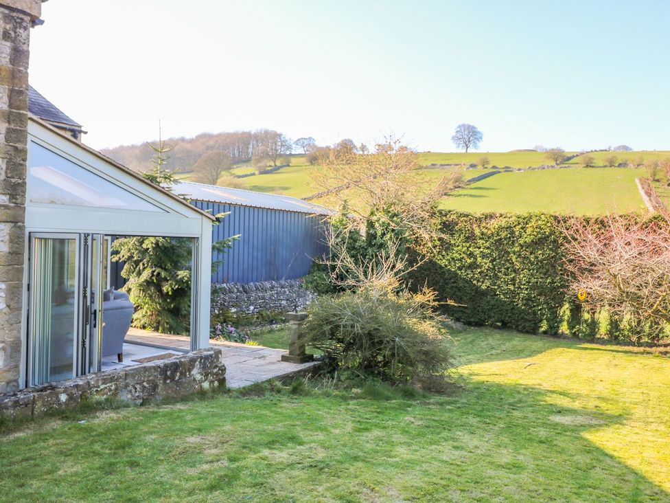 A garden with a glass conservatory and green hills at Peters Lea Bakewell