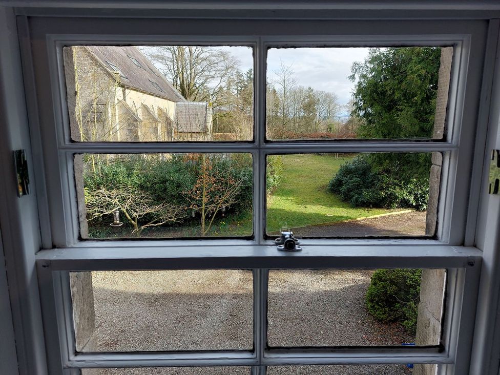 A view of a garden with trees and gravel from a window at The Coach House- Canonbie near Langholm