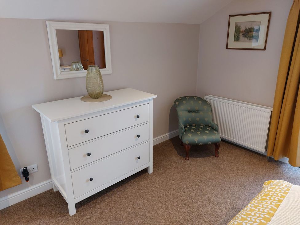 A bedroom with a dresser, chair and mirror at The Coach House- Canonbie near Langholm