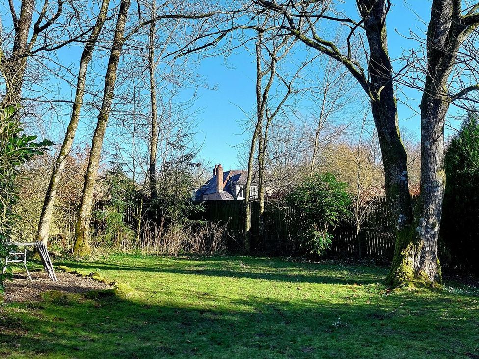 A garden with trees and a house in the background at The Coach House- Canonbie near Langholm