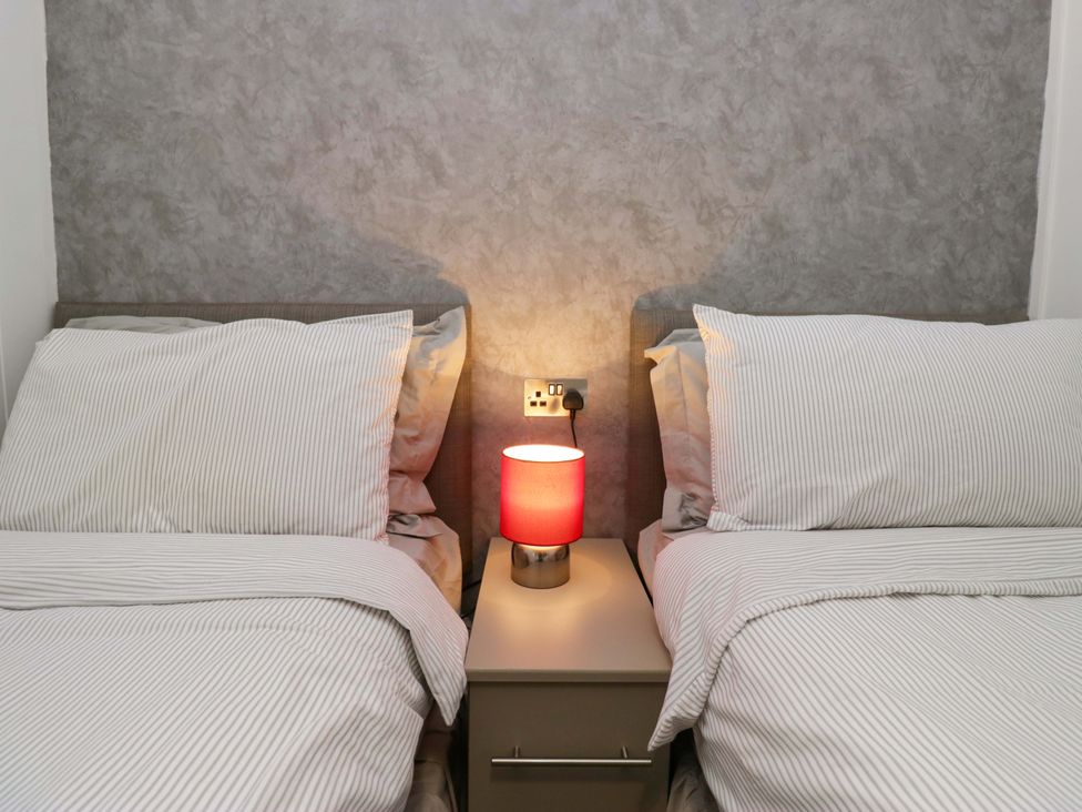 A bedroom with two beds and a lamp on a nightstand at 5 Waterside Wood Troutbeck Bridge