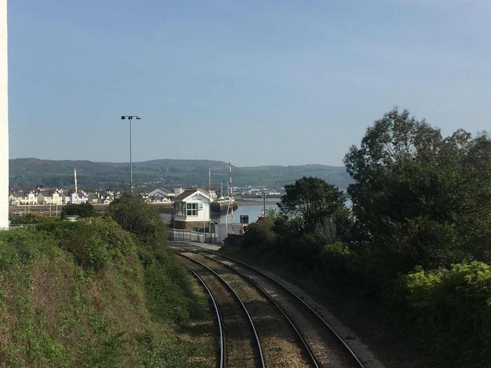 A view of train tracks leading to water and buildings at Heulfan - 17 Deganwy Castle Apartments in Deganwy