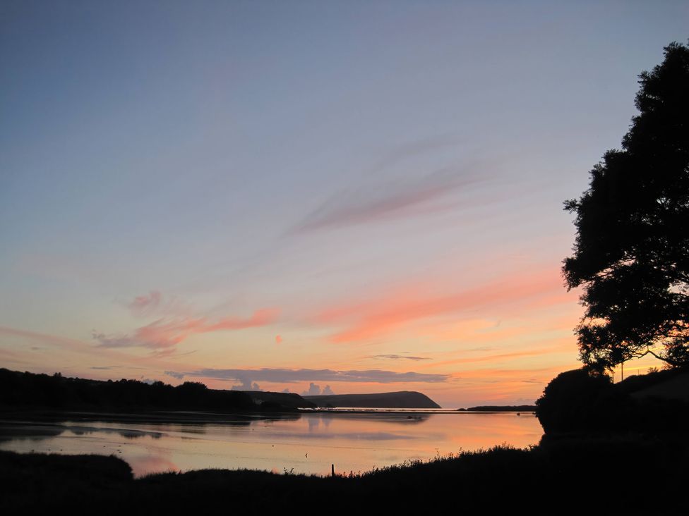 A sunset over water with clouds and trees at Bryncyn in Newport, Pembrokeshire