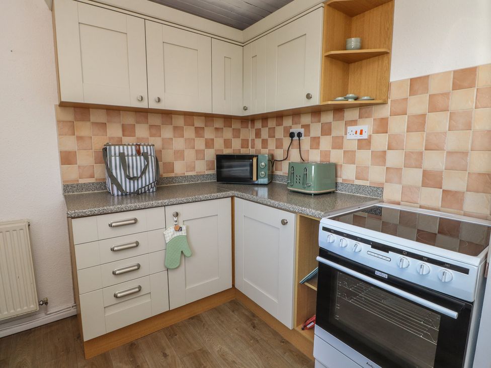 A kitchen with cabinets, stove, microwave, and kettle at Mona View in Amlwch