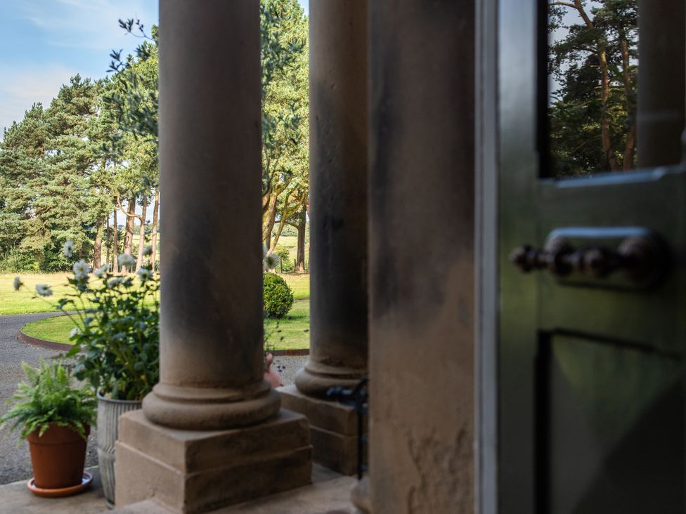 A view from a porch with pillars and plants leading to a garden at The Country House Cumbria, Castle Carrock