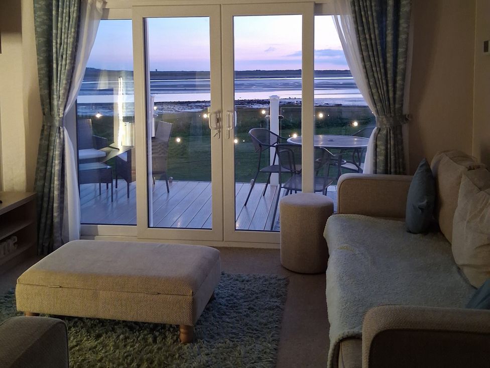 A living room with a sofa and footrest overlooking the deck at Willerby Malton 2023 in Kidwelly