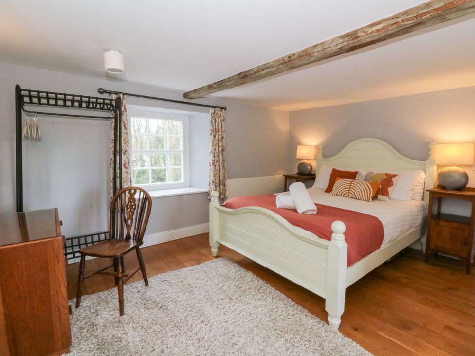 A bedroom with a bed, chair, and wardrobe at Secret Garden Cottage in Ciliau Aeron near Aberaeron