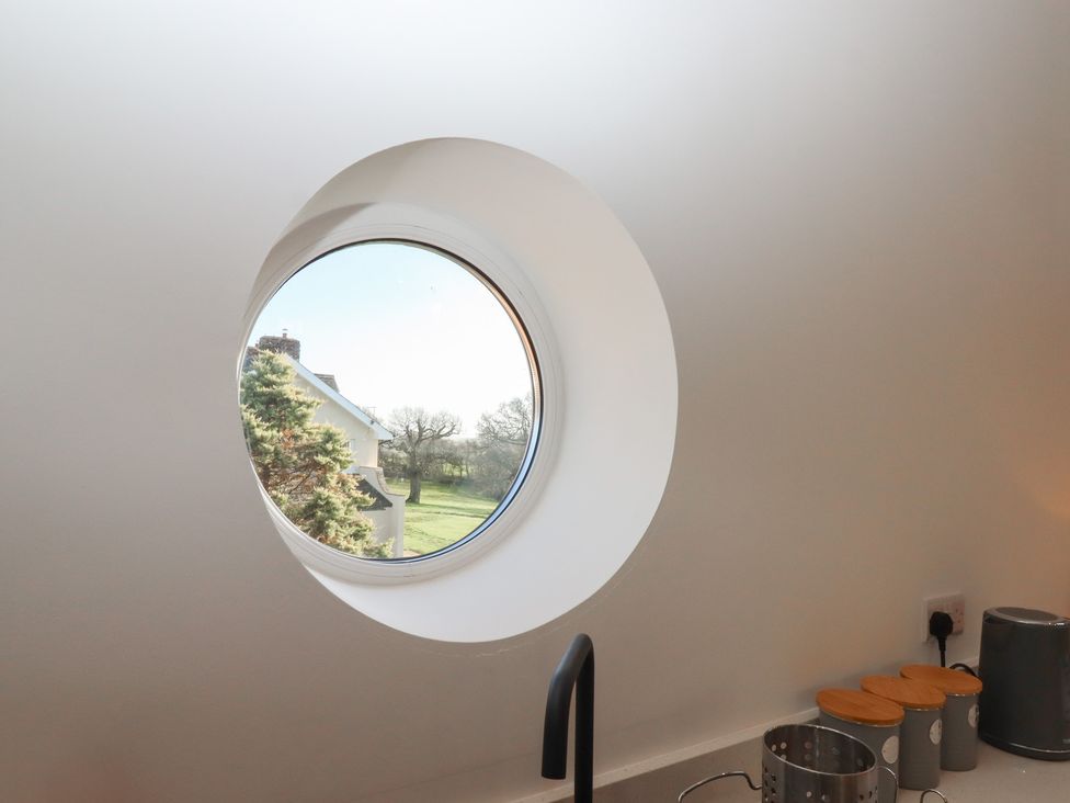 A circular window in a kitchen looking out to a garden at Hilldown Granary near Bow