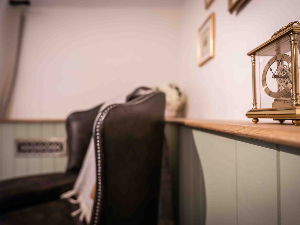 A living room with an armchair and clock at Freya's Cottage in Metheringham