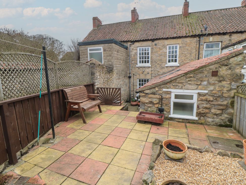 A garden with a stone wall and a wooden bench at Daisy cottage in Pickering