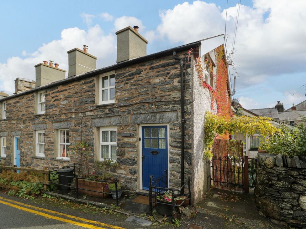 An outdoor view of a stone house with a blue door and flowers at Noddfa Penmachno