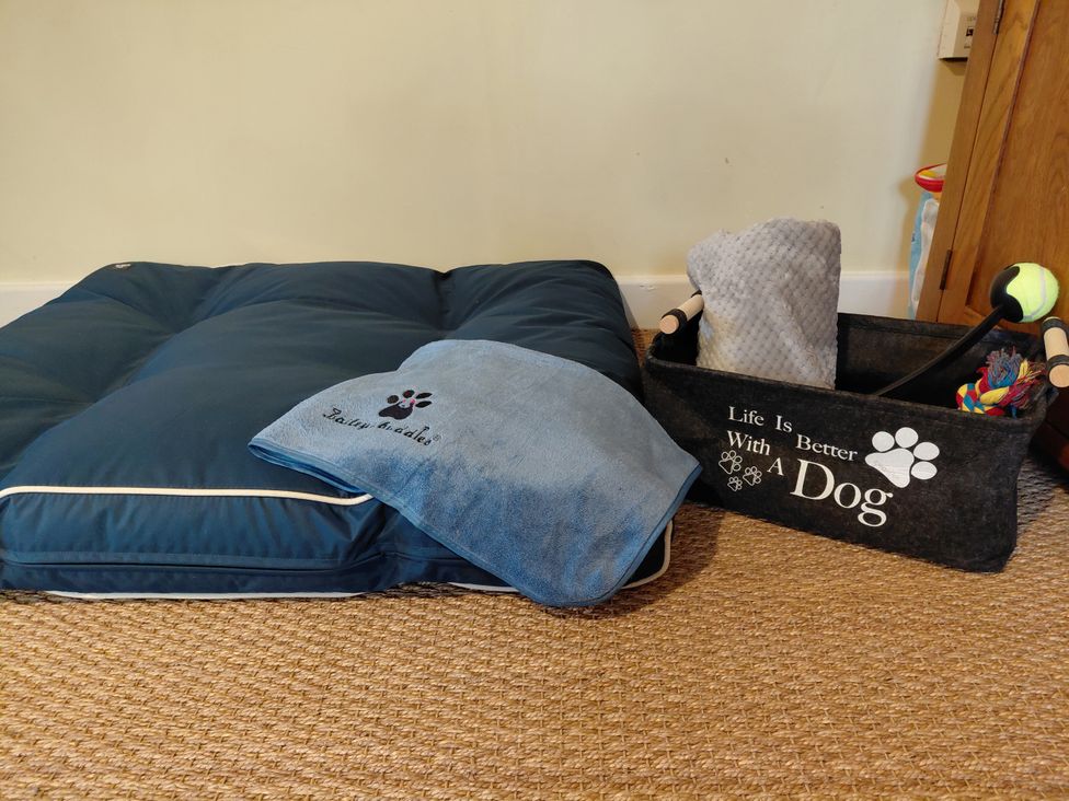 A dog bed with a blanket and a basket of toys at Noddfa, Penmachno