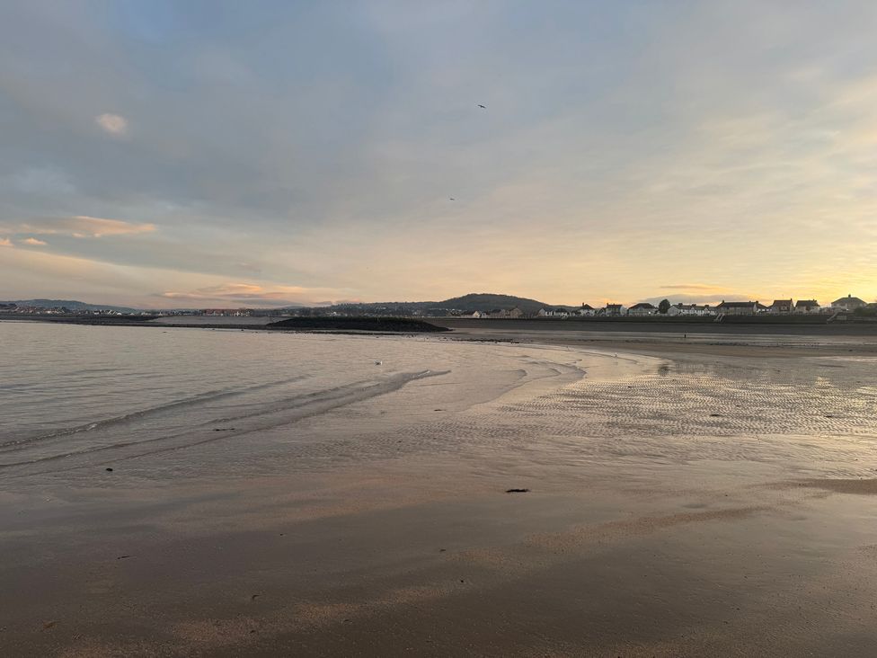 A beach with water and houses in the background at The Hideaway in Penrhyn Bay