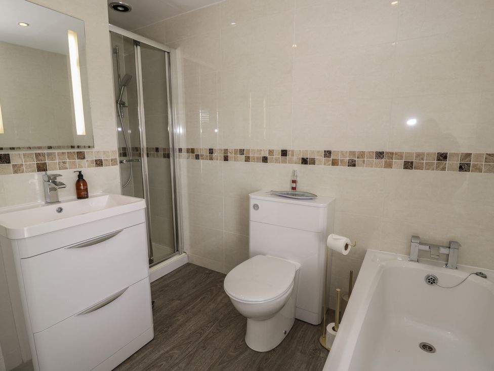 A bathroom with a shower, toilet, bath, and sink at The Hideaway Penrhyn Bay