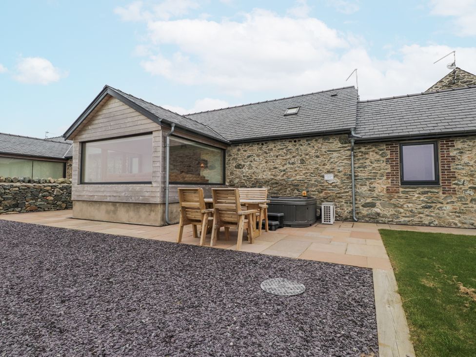 An outdoor area with a patio, wooden table, and hot tub at 2 Trem Y Mor in Llanfwrog near Llanfachraeth