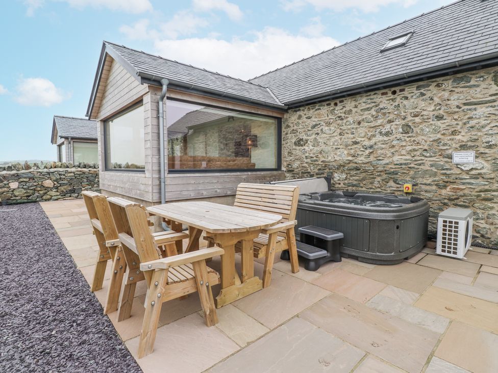 An outdoor area with a hot tub and wooden furniture at 2 Trem Y Mor Llanfwrog near Llanfachraeth
