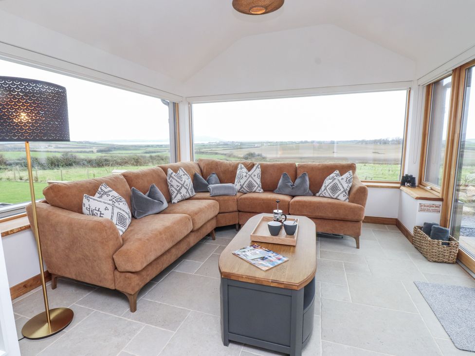A conservatory with a brown sofa and a coffee table at 2 Trem Y Mor Llanfwrog near Llanfachraeth