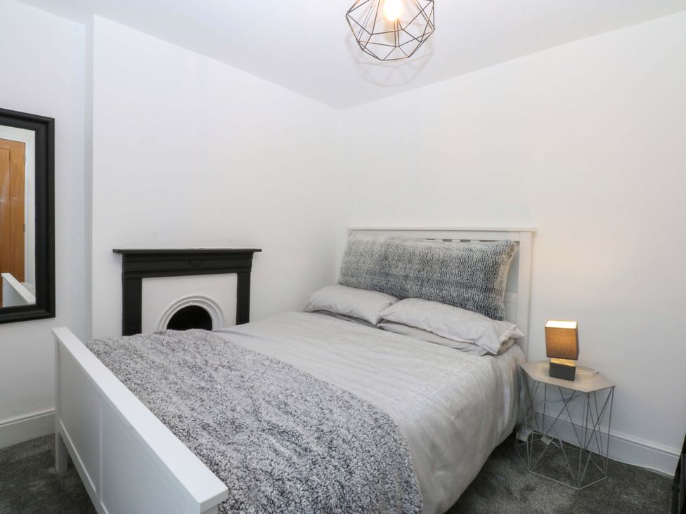 A bedroom with a bed, lamp, fireplace, and mirror at 4 Brynteg Terrace Menai Bridge
