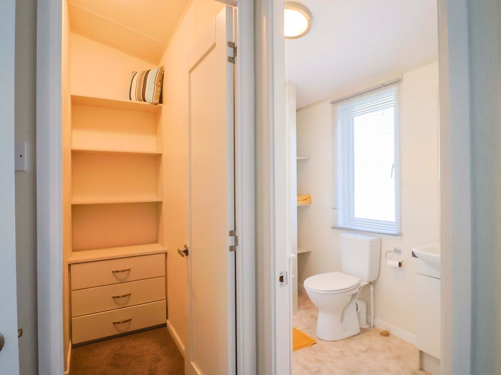 A bathroom with a toilet, sink, and shelves at 91 Swanage Coastal Park in Swanage