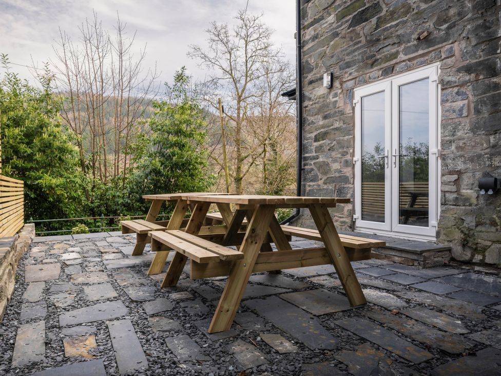 A patio with a wooden table and stone wall at Green Bank in Betws-Y-Coed