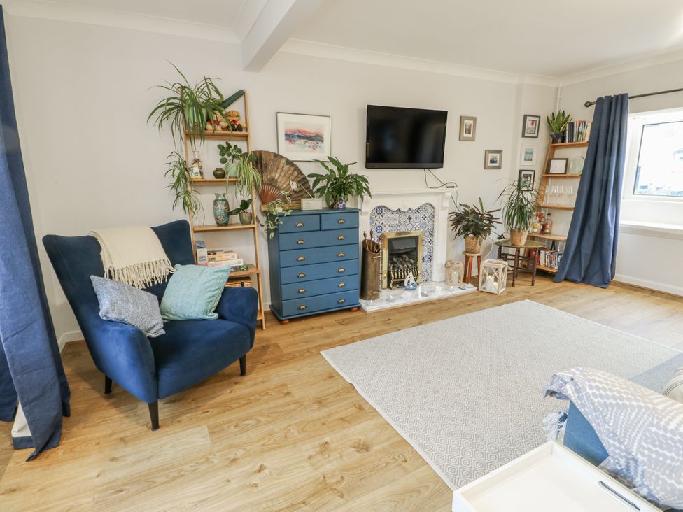 A living room with a television and blue armchair at 16 Ffordd Meigan in Beaumaris