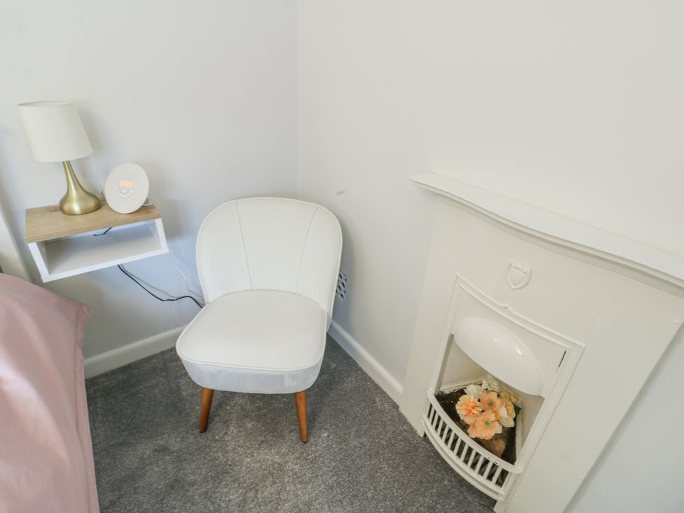A bedroom with a chair near a lamp and a fireplace at 16 Ffordd Meigan Beaumaris
