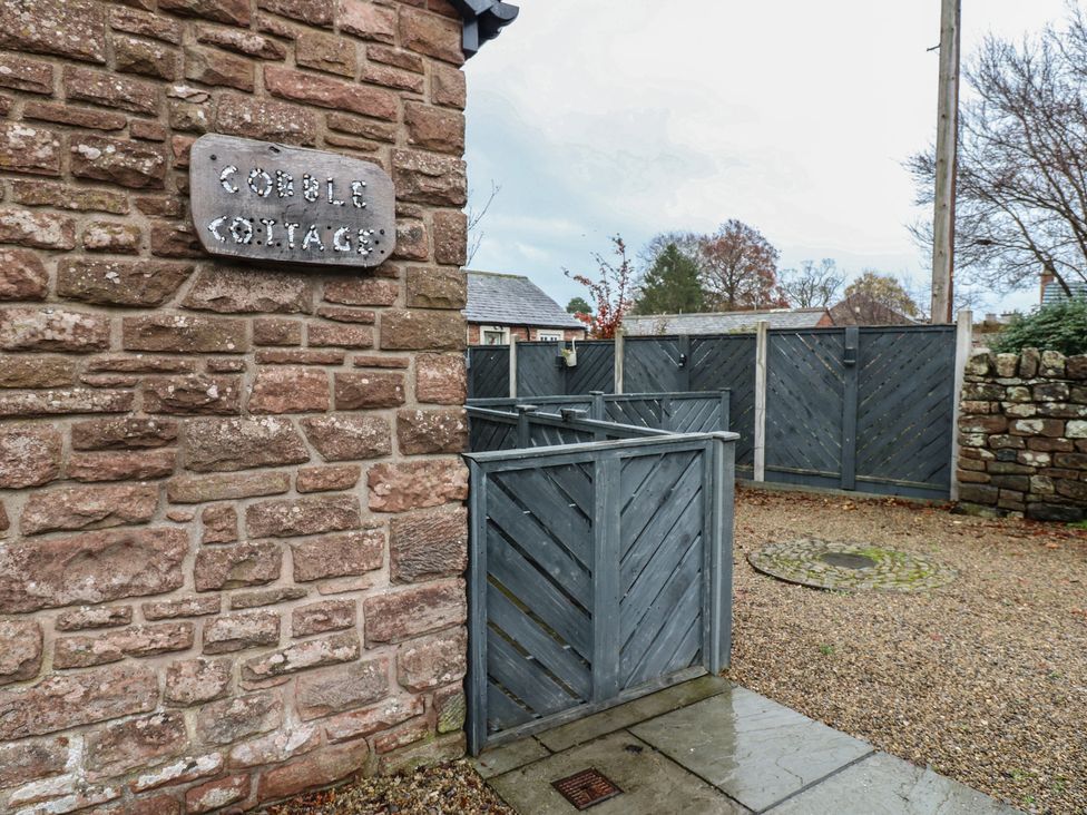 An outdoor area with a sign and stone wall at Cobble Cottage Long Marton near Appleby-In-Westmorland