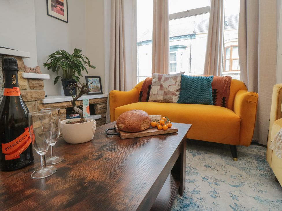 A living room with a yellow couch, coffee table, and bottle of prosecco at Captain Jacks in Whitby