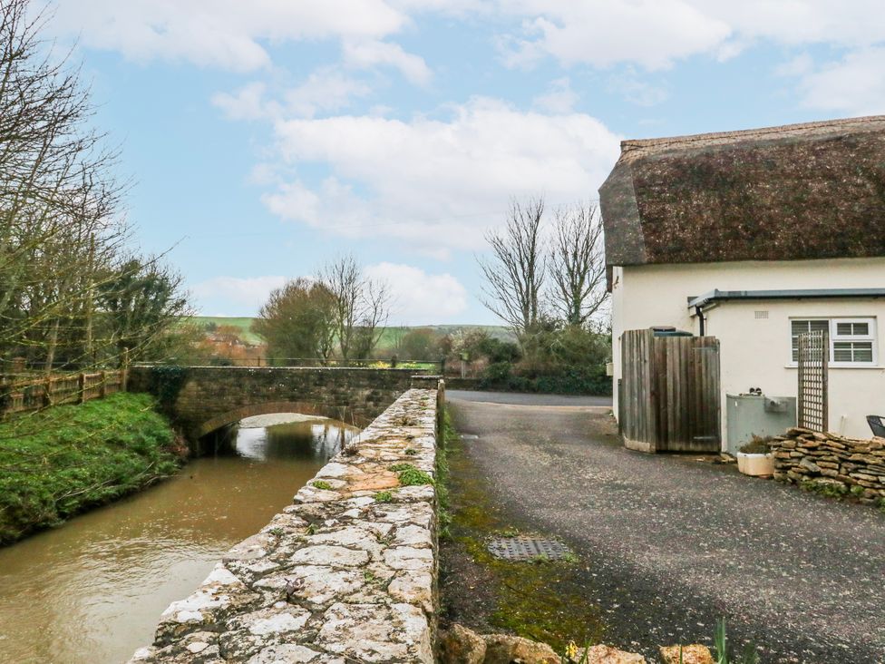An outdoor scene with a bridge over water next to a house at Long Barn in Burton Bradstock